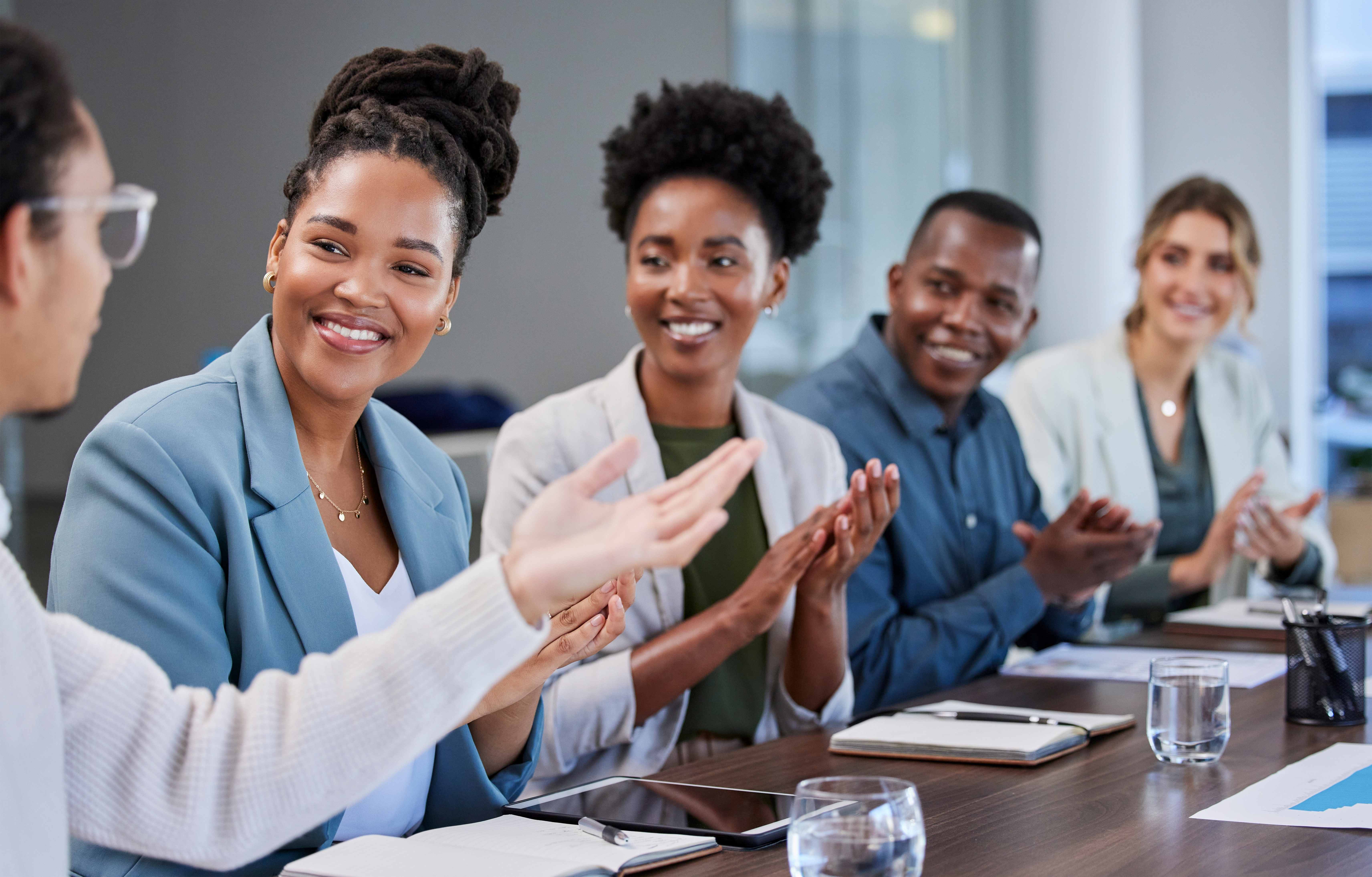 three black women and one black man seated at a table looking on at black woman at the head of the table