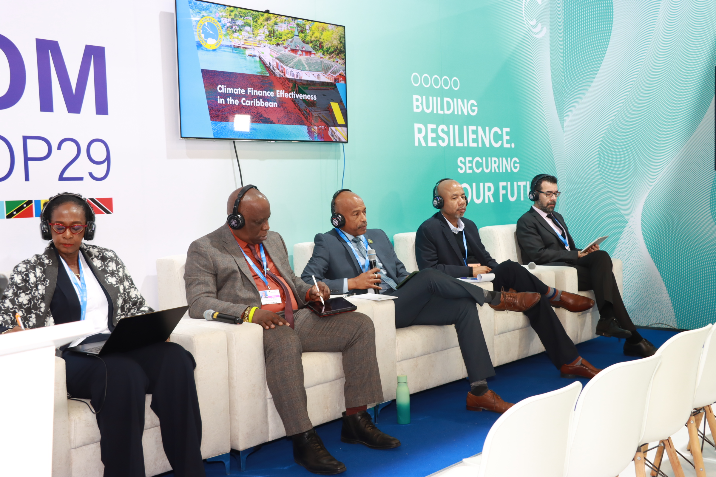 one woman and three men in business suits seated on stage on white lounge chairs 