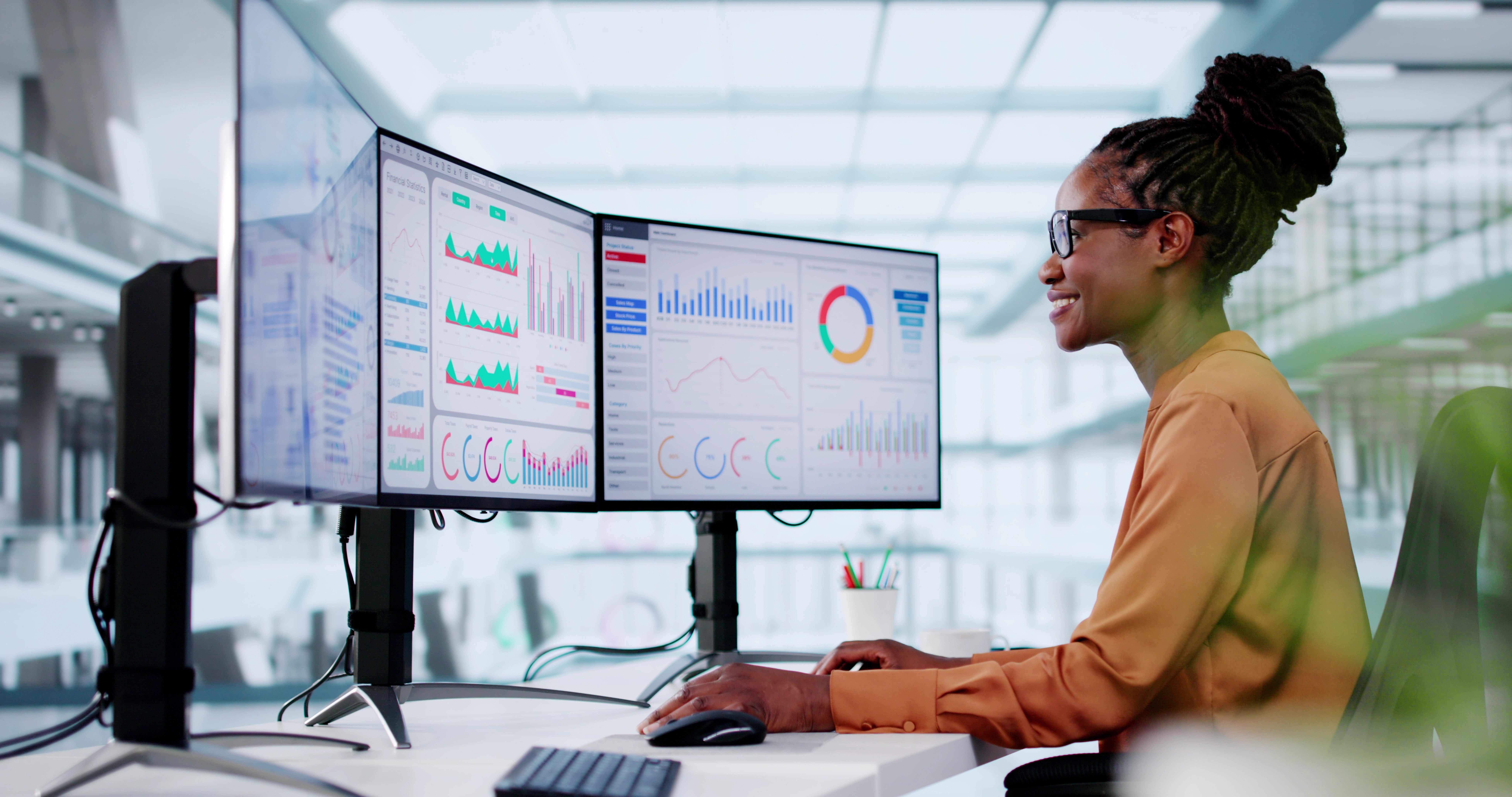 black woman sitting in front of screens smiling and looking at data 