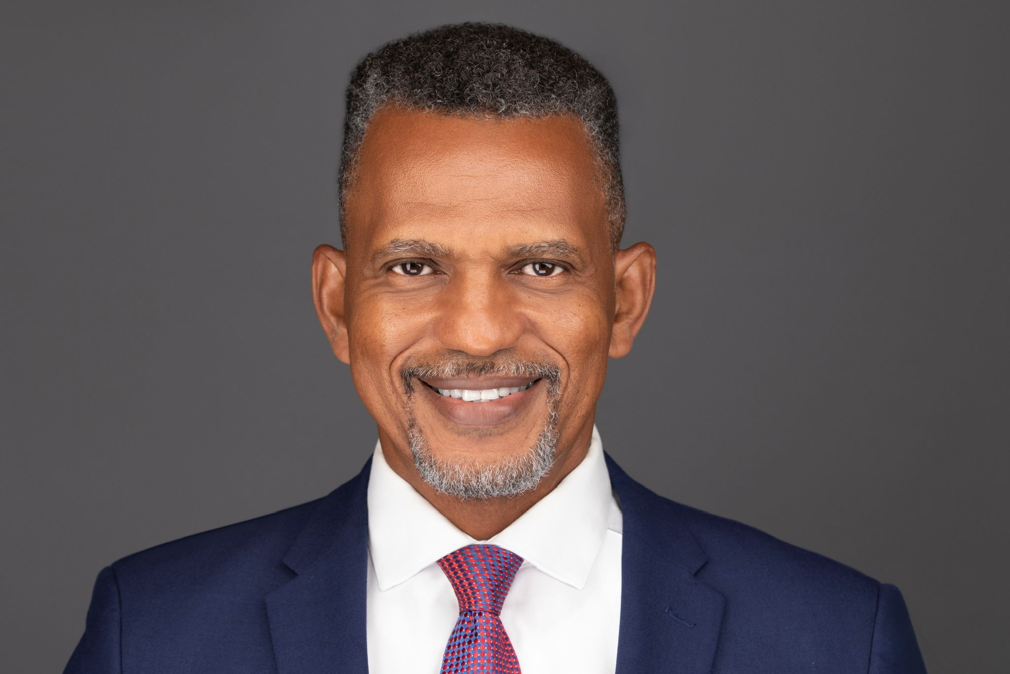 Daniel in dark blue suit with burgundy tie and white shirt, smiling looking into camera