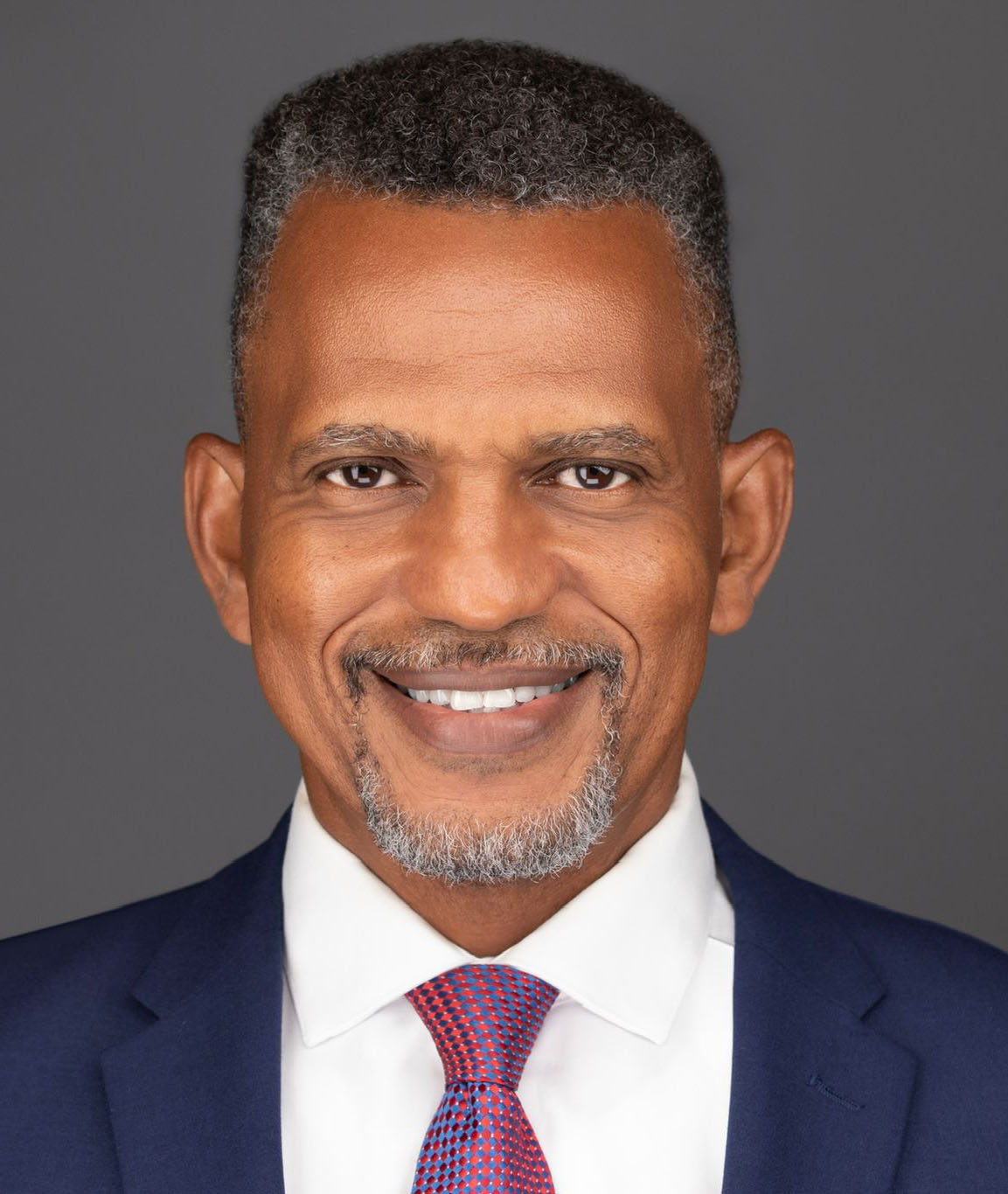 Daniel in dark blue suit with burgundy tie and white shirt, smiling looking into camera