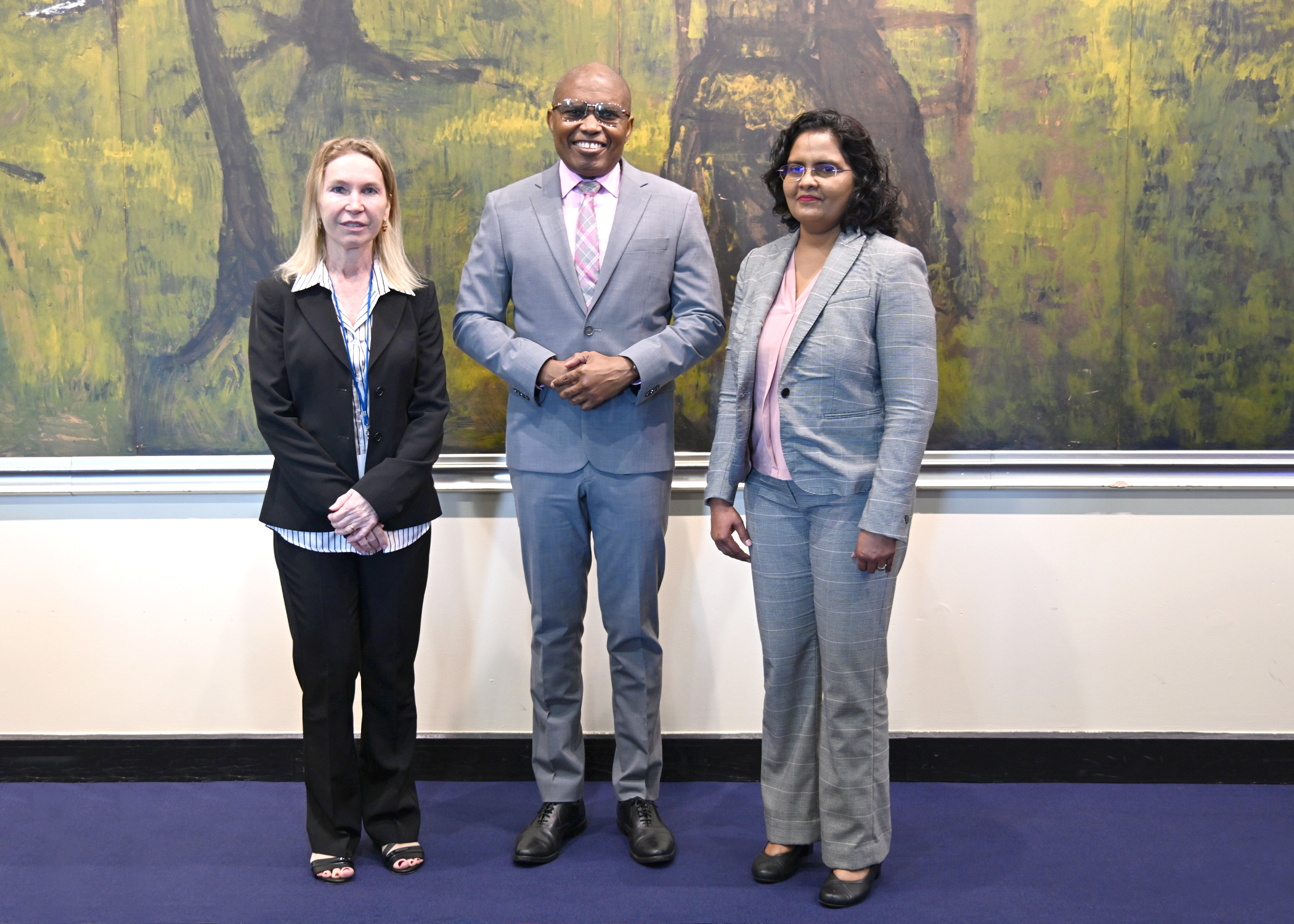 Two women flanking one man all in business suits standing in front a lightly coloured textured wall