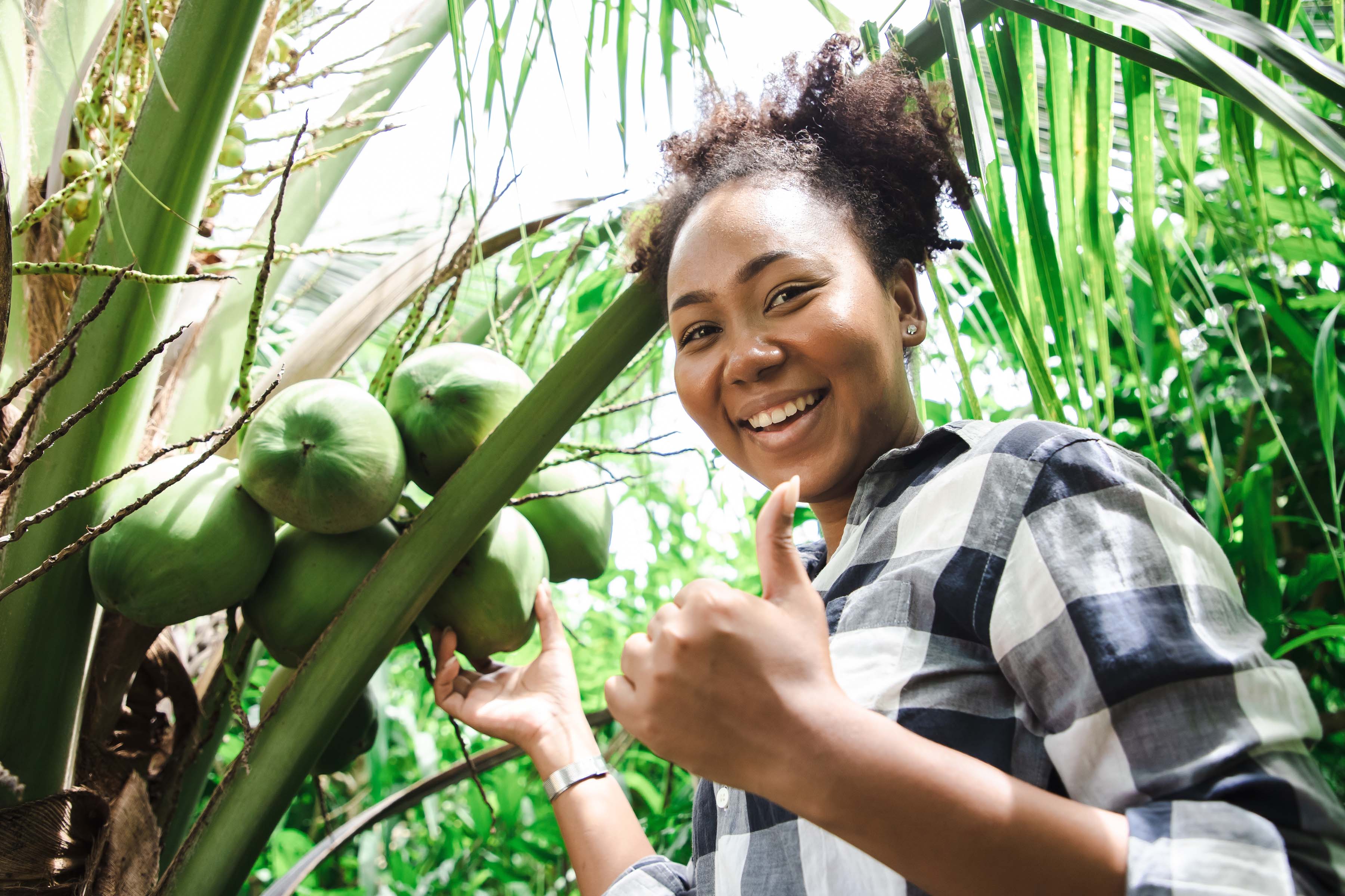 teenage black girl in coconut tree grove smiling into camera giving thumbs up