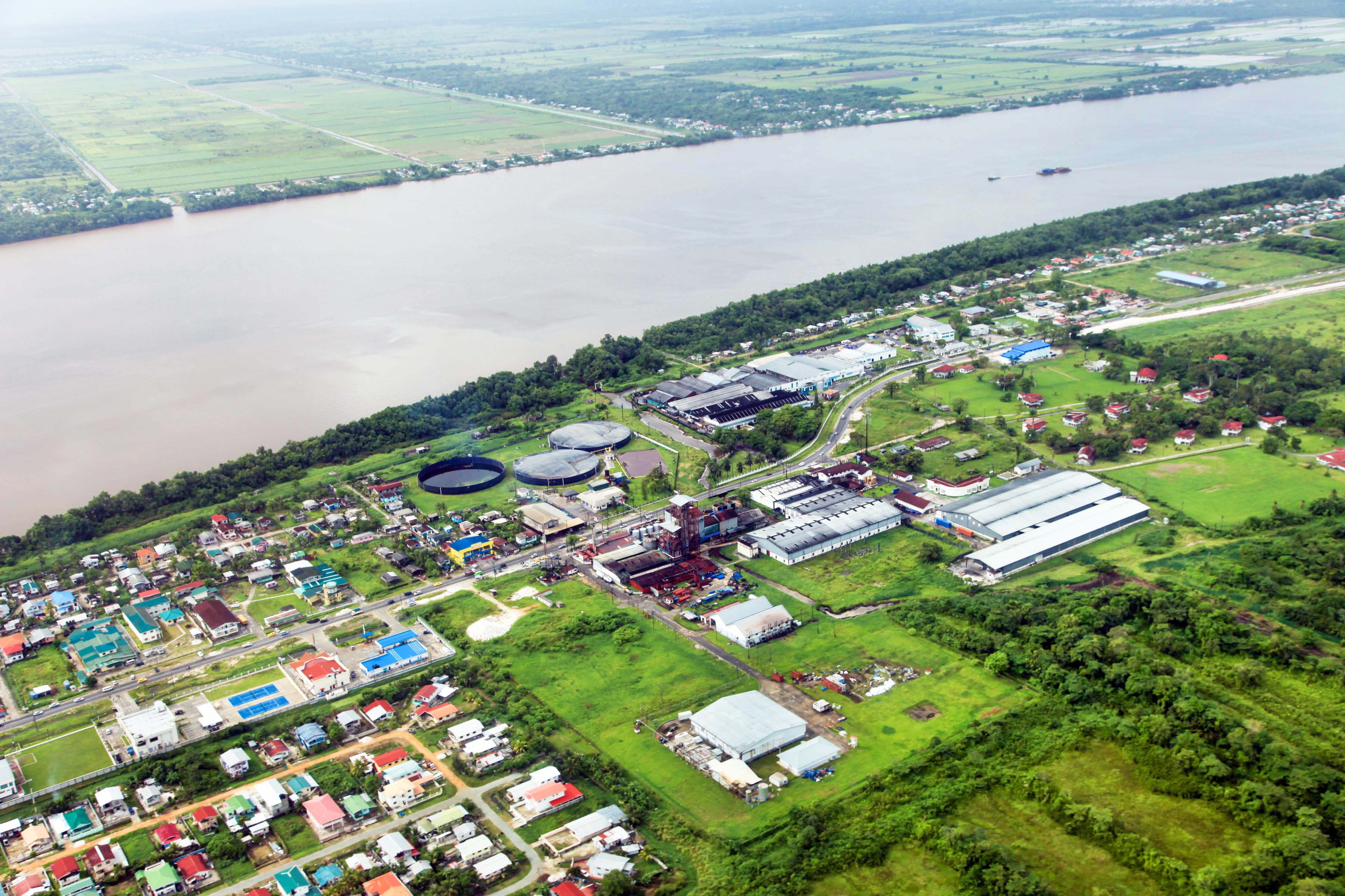 arial shot of coastal town with many green spaces with wide river running next to it