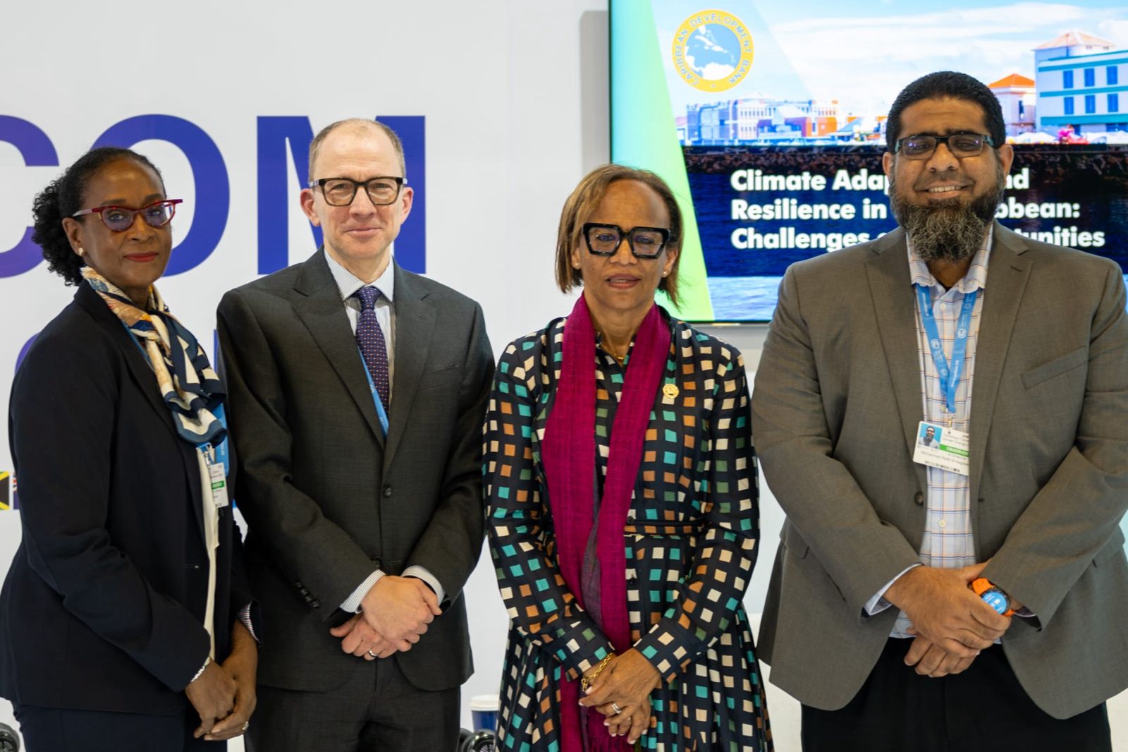 group photo of two men and two men in business attire standing in front of a CARICOM COP 29 backdrop