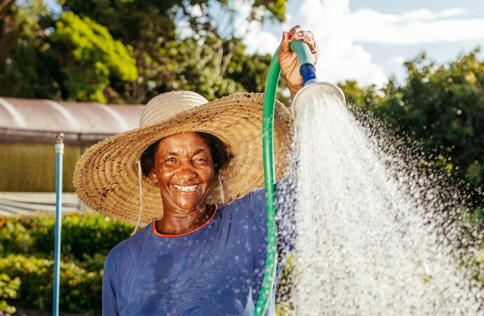 black woman in straw hat with running water hose in hands