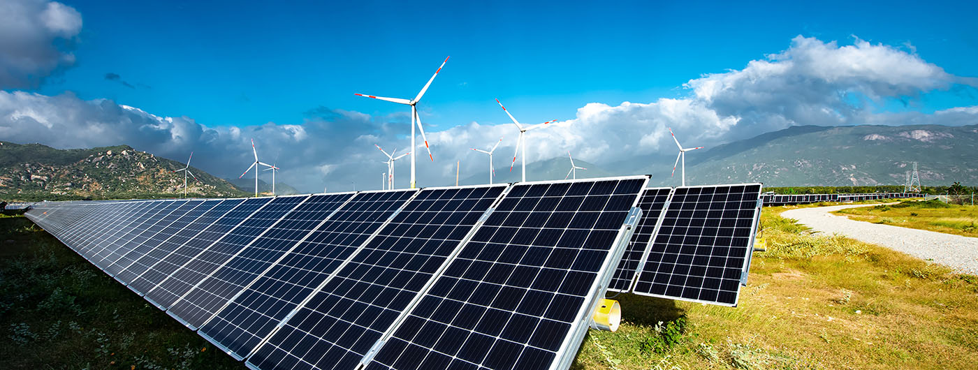 Solar panels farm under blue sky with wind turbines in the background