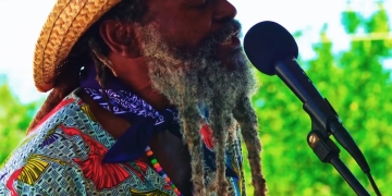 Rastafarian man in straw hat with a dreadlock beard singing in front of a microphone