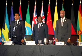 Three men, including CDB Vice President of Finance, Gregory Hill, CDB Acting President Isaac Solomon and Chairman of CDB's Board of Governor's Hon. Ahmed Hussen stand on a platform in front of several flags 