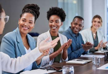 three black women and one black man seated at a table looking on at black woman at the head of the table