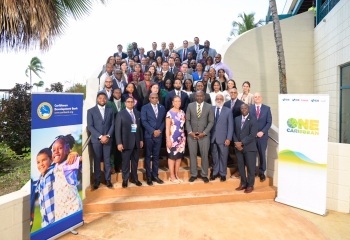 Large group of delegates standing on stairs outdoors in business attire flanked by two banners