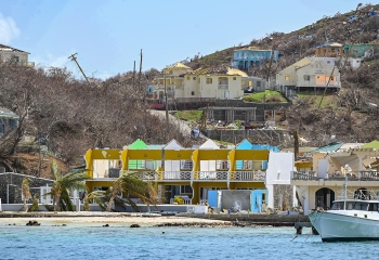 buildings along tropical coastline with roofs missing and other structural damage as caused by high force hurricane winds