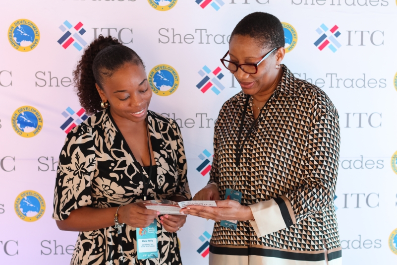 two black women in front a branded backdrop sharing and reading an opened brochure