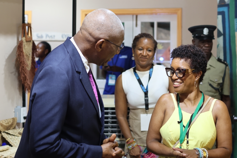 a black man in a blue suit speaking to a woman in a yellow sleeveless dress 