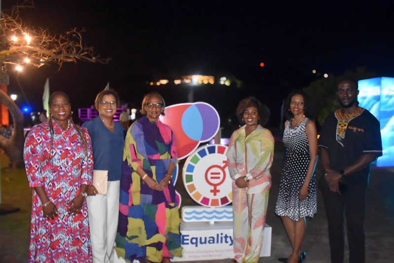 six black persons standing at night flanking the Gender Equality Village sign 