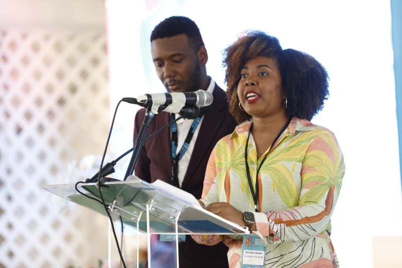 a man in a black suit and a woman with an afro in bright floral patterned dress speaking at a leactern