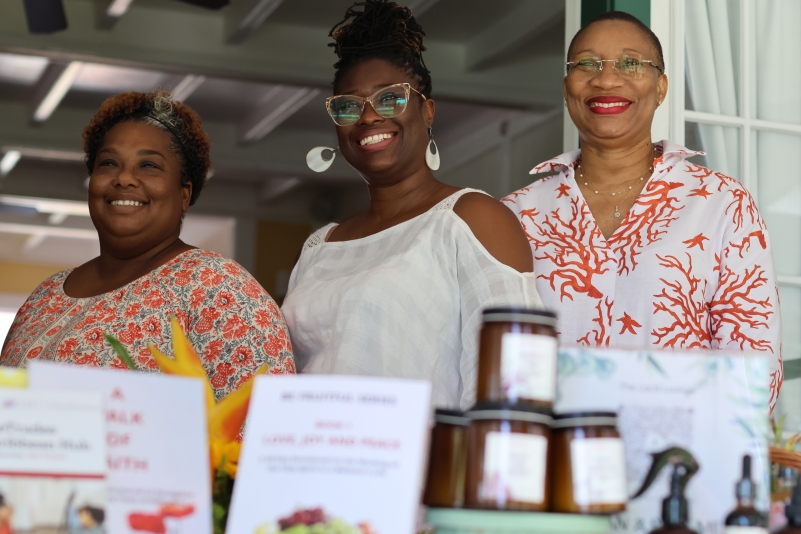 three black women standing behind a table of products smiling 