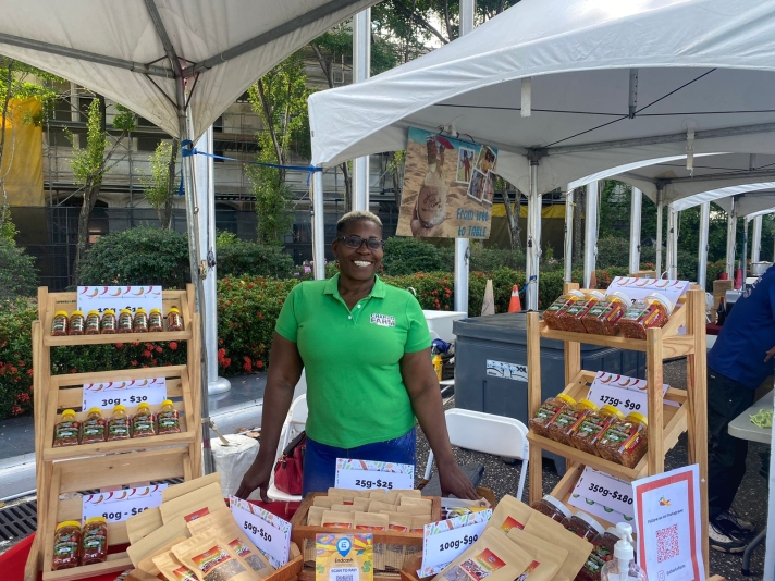 black woman in green shirt standing under a tent with agri processed products on display